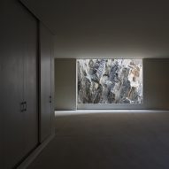 An empty, dimly lit room with a floor-to-ceiling window looking onto rocky terrain