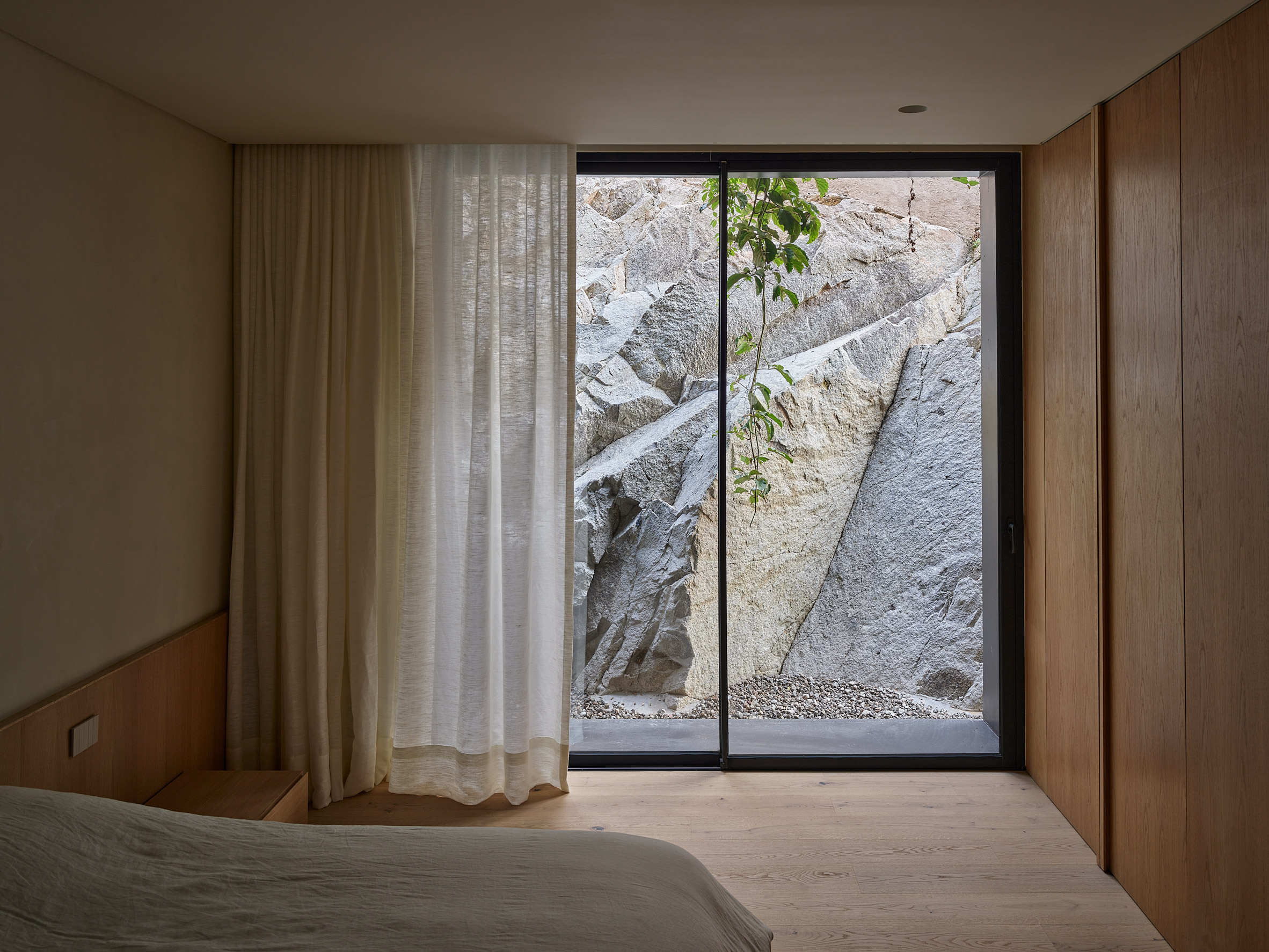 Warm-toned bedroom with timber wardrobe and floor-to-ceiling windows looking onto rocky terrain