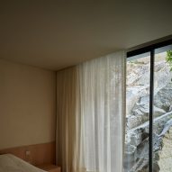 Bedroom with sheer curtains and floor-to-ceiling windows looking onto rocks