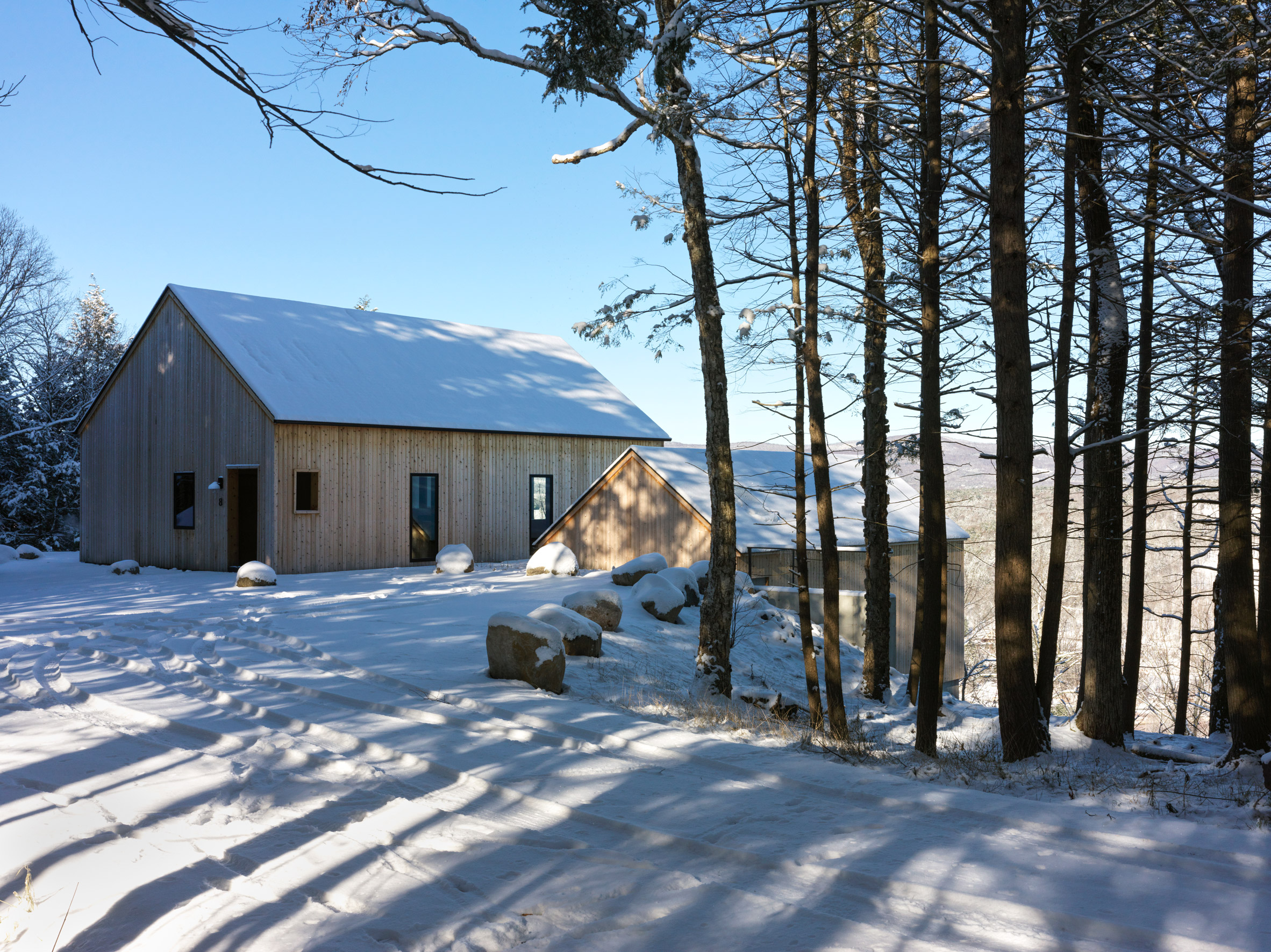 Two timber-clad pitched-roof structures on a snowy hill with trees