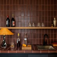 Kitchen counter and wall tiles with brown rectangle tiles, with black units and a wooden shelf