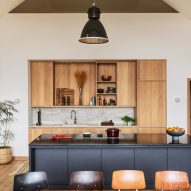 Open-plan kitchen and dining room with wooden table, black kitchen island, timber kitchen storage and exposed roof structure