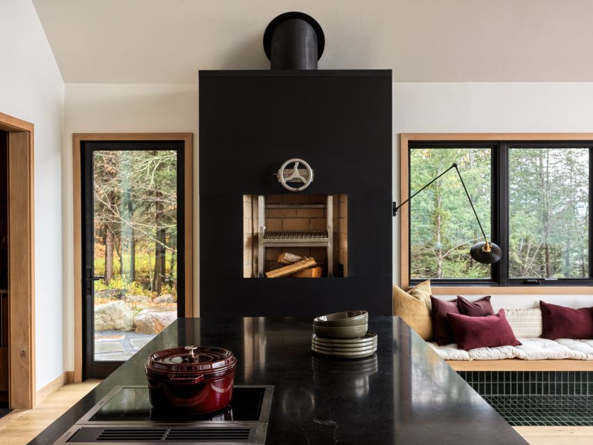 A kitchen with white walls, black island top and a black fireplace next to built-in seat under a window