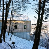 Concrete and timber-clad home on a snowy hillside in a wooded area