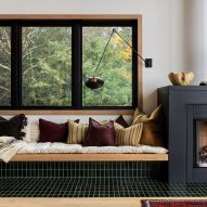 Built-in seating covered in black tiles under a window, with cream blankets and yellow and purple cushions next to a fireplace