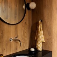 Black bathroom sink with circular wall mirror and timber walls