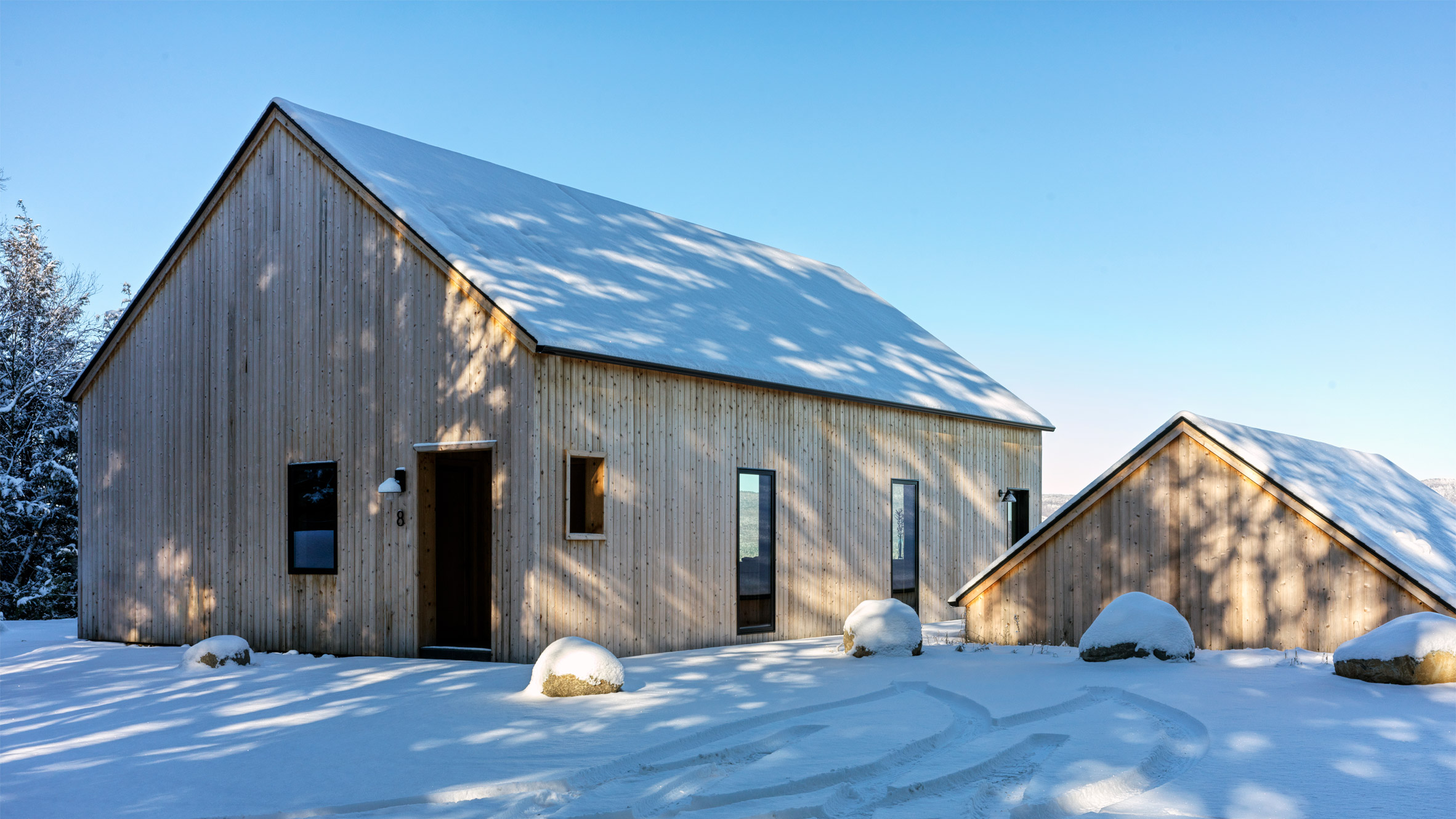 Two timber-clad pitched-roof structures on a snowy hill