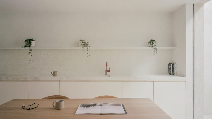 Minimalist white kitchen a white stone worktop, white shelf and wooden dining table and chairs