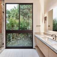 White bathroom with marble countertop and large window overlooking a garden
