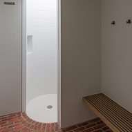 White bathroom with brick floor, circular shower and wood bench