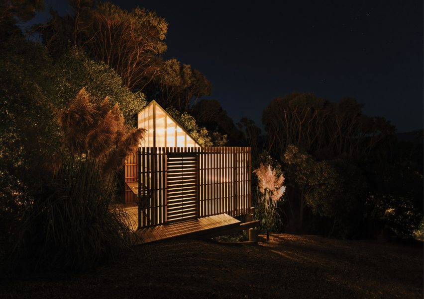 Mono-pitched polycarbonate shed on a wooden deck shining light through timber slats on a slope in the New Zealand bush
