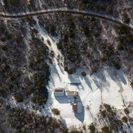 Aerial view of a home made up of three cabins in a snowy clearing in a forest