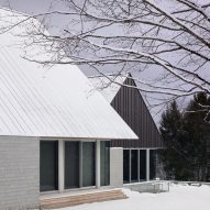 Two cabins with granite walls and metal roofs in a snowy clearing with trees