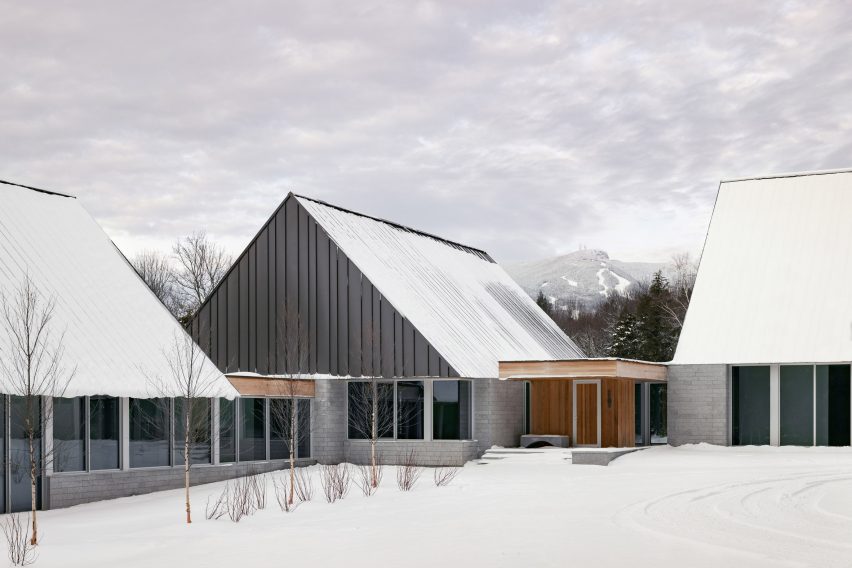 A series of pitched-roof structures with granite stone walls and metal-clad gable ends on a snowy mountainside
