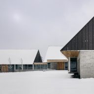 Three cabin structures with granite walls and metal-clad gable ends connected by glazed walkways on a snowy mountainside