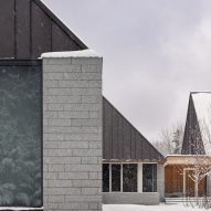 Three cabin structures with granite walls and metal-clad gable ends in a snowy clearing