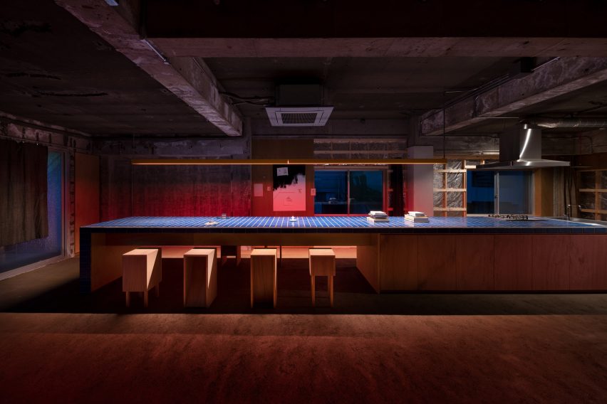 Banco de isla de cocina largo rematado con azulejos azules en un apartamento industrial con poca luz