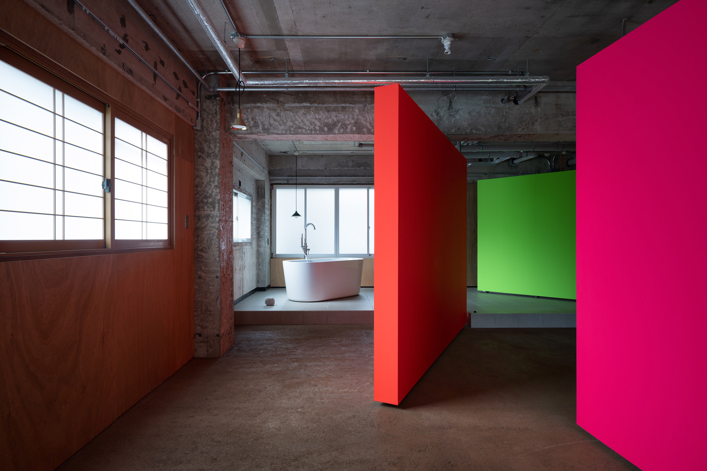Fluorescent rotating partition walls revealing a freestanding bathtub in a concrete apartment