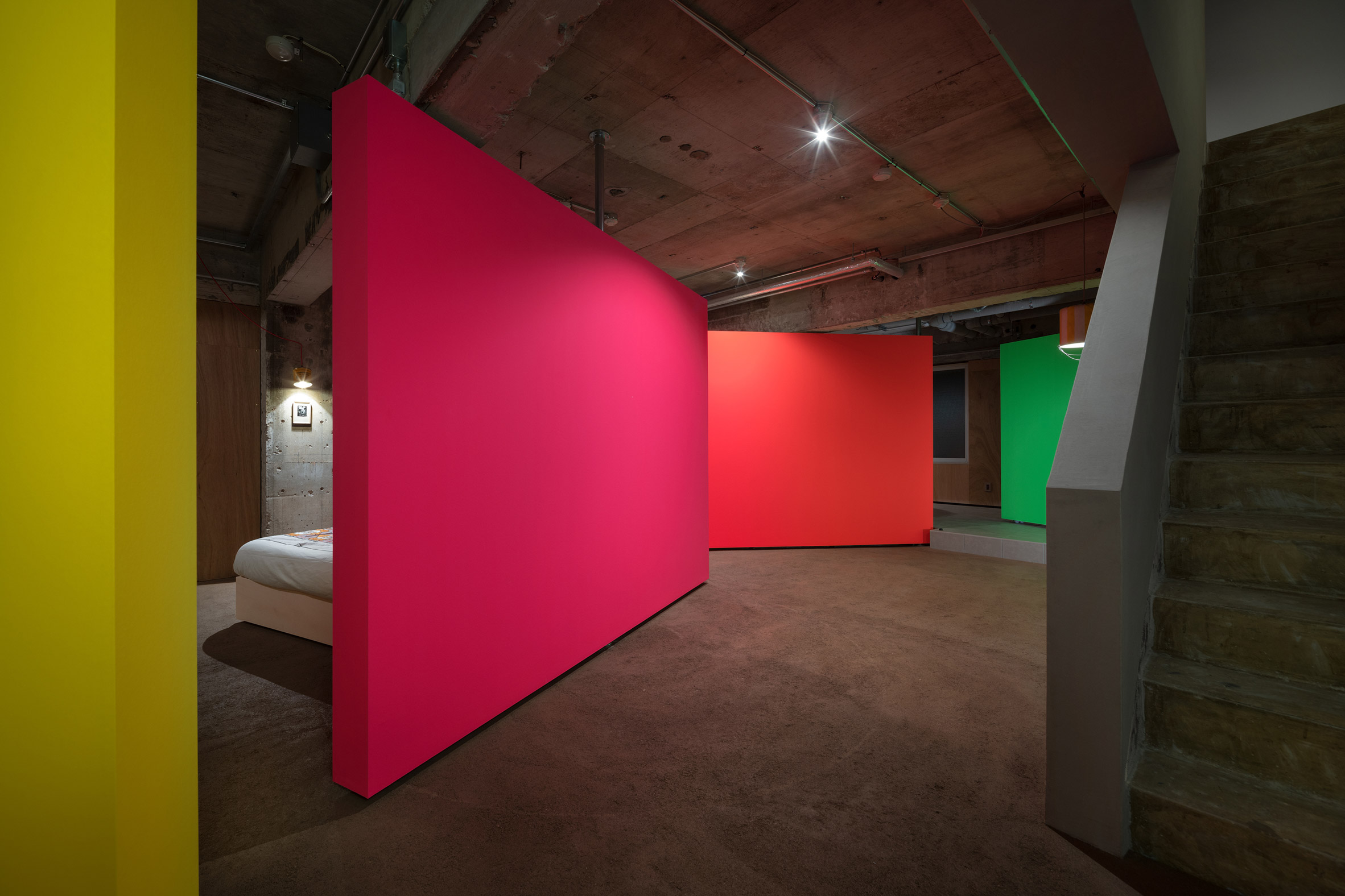 Yellow, pink, orange and green rotating partition walls zoning a bedroom in a concrete apartment by Ab Rogers Design