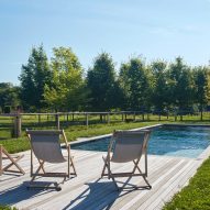Outdoor swimming pool in a grassy garden with with timber decking and three deck chairs