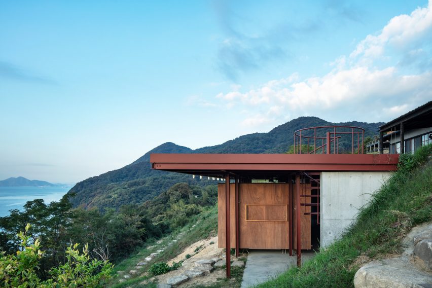 One-storey building with a red steel frame and concrete and wood walls extending out of a hillside