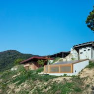 A bunker-style building is a sloped roof and a guesthouse with a red steel frame built into a hillside