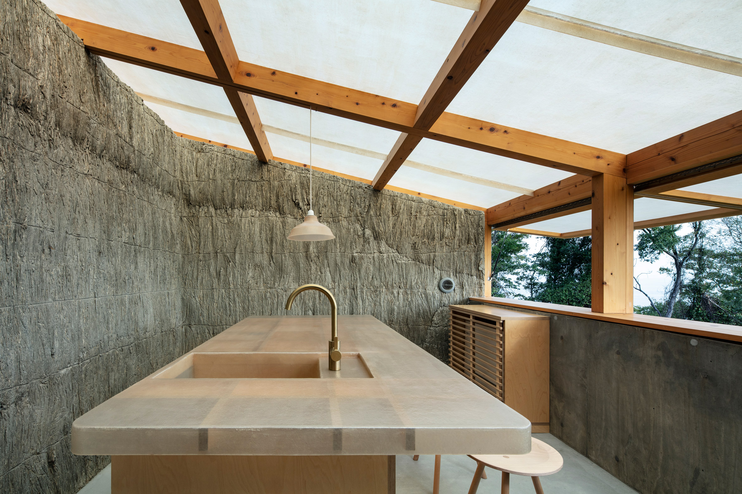 Interior of a kitchen space with a sloped translucent roof, textured walls and a large central island with a sink