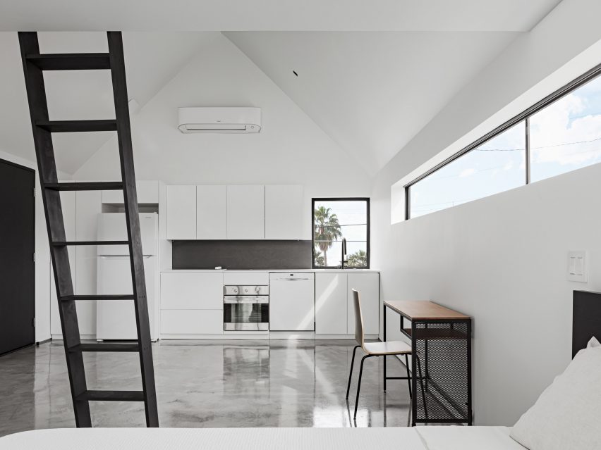 Kitchen view of all-white apartment with black ladder