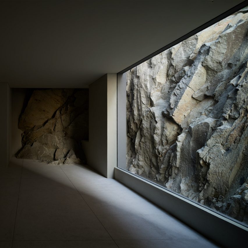 A dark empty room with floor-to-ceiling window looking onto rocky terrain
