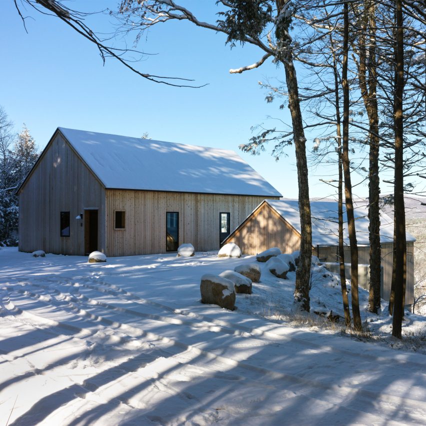 Two timber-clad pitched-roof structures on a snowy hill with trees