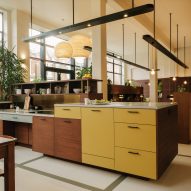 Kitchen island with wood and yellow-painted cupboard doors in an open-plan office with overhead pendant lamps