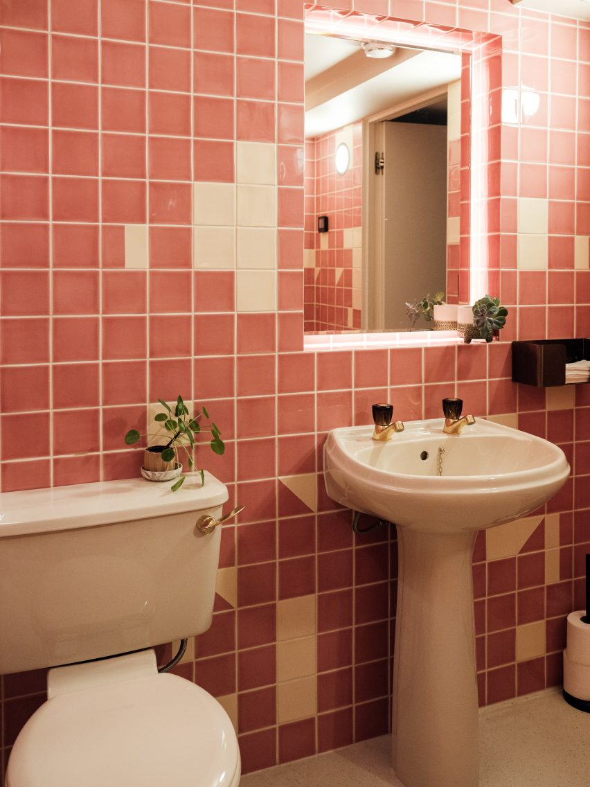 Cuarto de baño con lavabo e inodoro blancos y pared de azulejos blancos y rosas en el interior de la oficina de The Mint List
