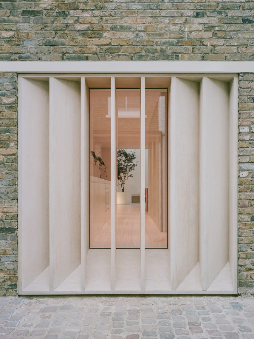 Rejillas de madera a medida en una casa de ladrillo frente a una gran ventana que da a una cocina blanca