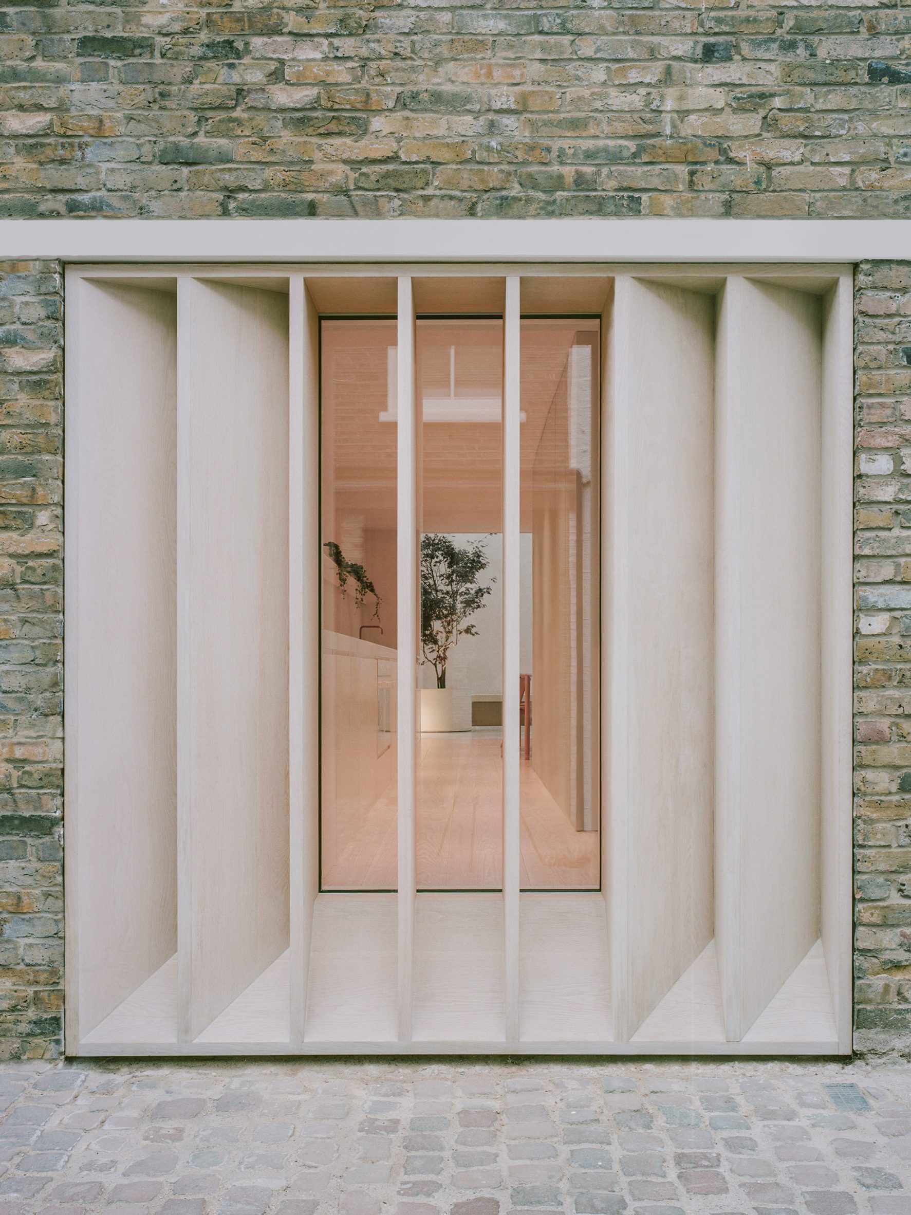 Bespoke timber louvres on a brick home in front of a large window looking into a white kitchen