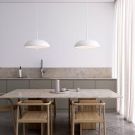 Two white pendant lamps suspended over a stone table with wooden chairs in a kitchen with khaki cupboard doors