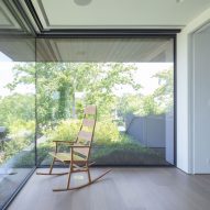 Wooden rocking chair in a room with wooden floors in front of a large corner window overlooking greenery