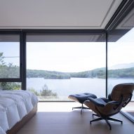 Lounge chair, foot stool and bed in a bedroom with a large corner window overlooking a lake