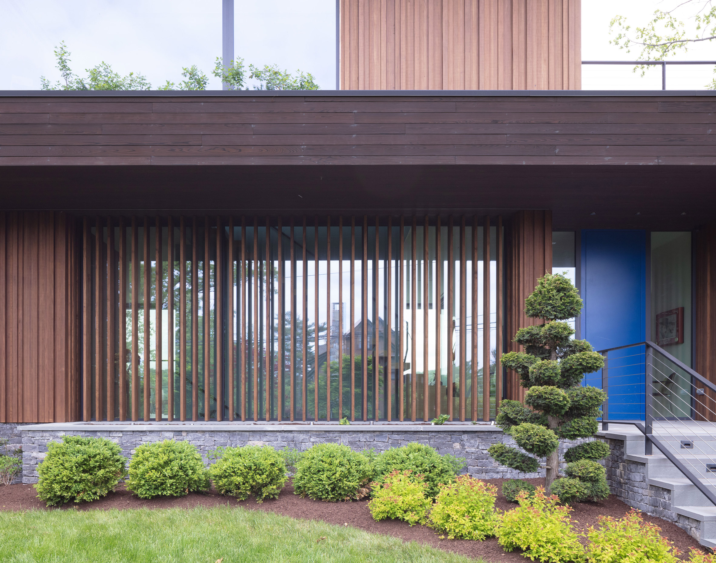 Timber cladding over glazing on a house with a front garden