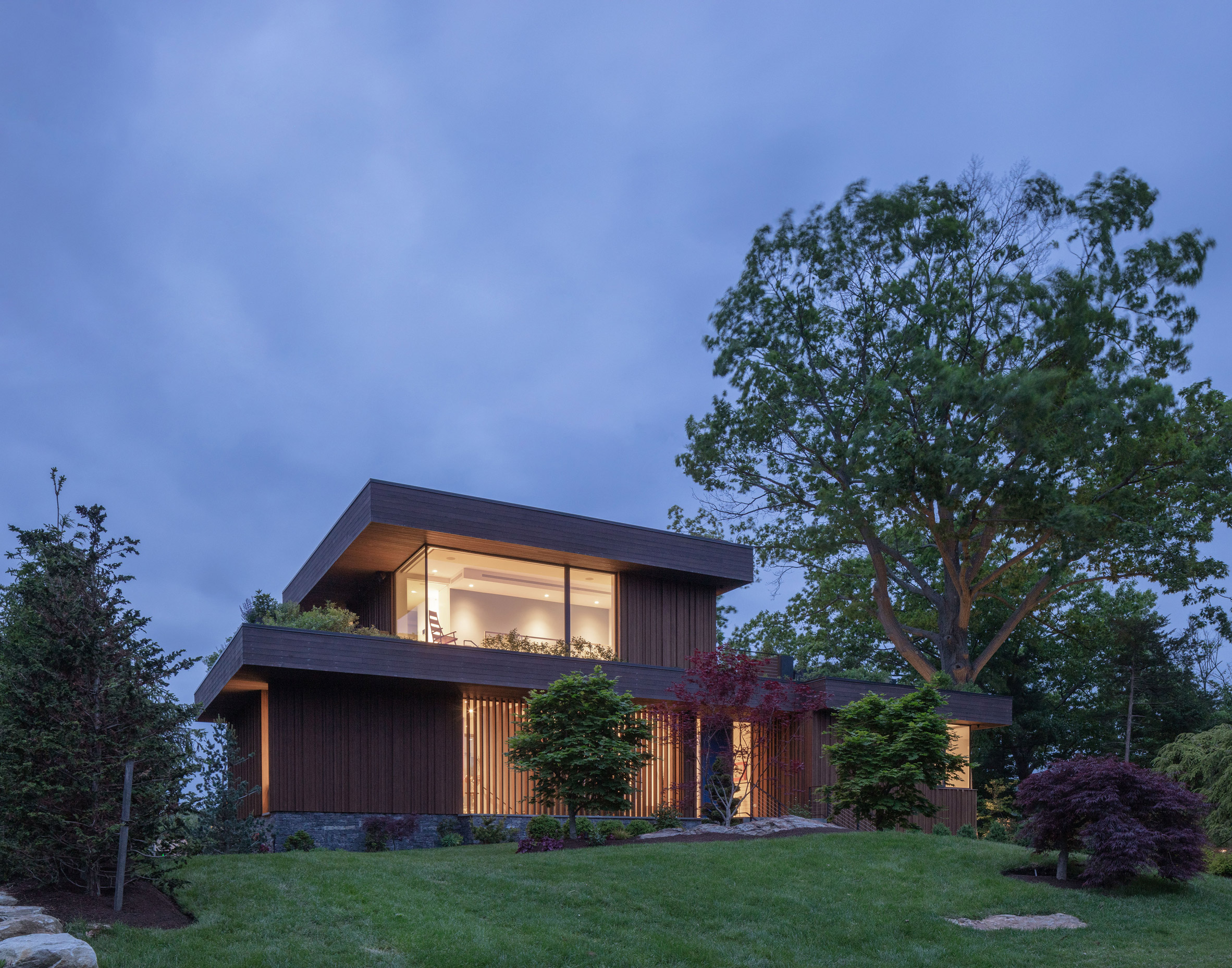 Exterior of a two-storey timber-clad lake house with front lawn by Worrell Yeung