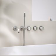 Chrome wall-mounted bath taps, handles and shower head next to a bath