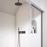 Black metallic wall-mounted shower head and handles in a cream-tiled shower