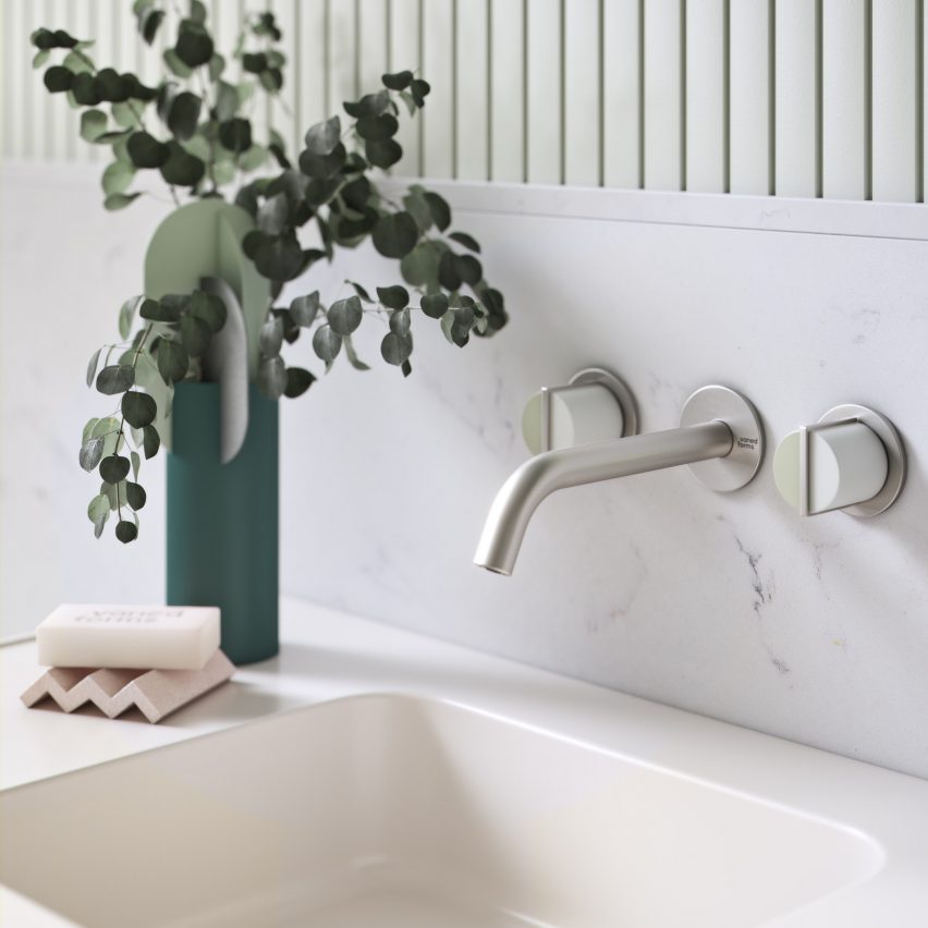 Chrome-plated wall-mounted faucet above a cream-colored washbasin with a vase of leaves