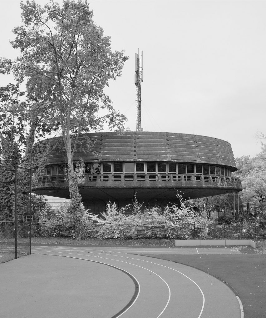 Black and white photo of a circular concrete brutalist building on a street with trees
