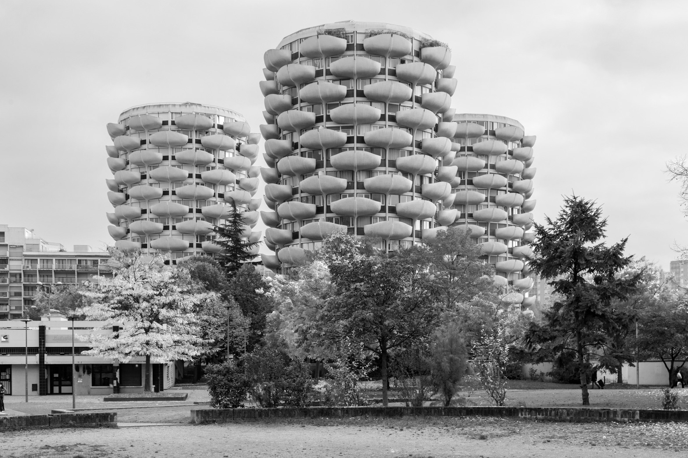 Black and white photo of three cylindrical multi-storey brutalist buildings with curved balconies staggered on the exterior