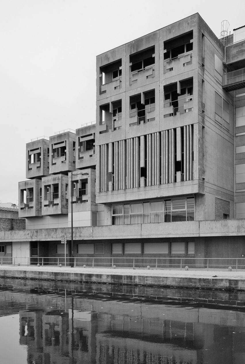 Черно-белое фото прямоугольного бруталистского бетонного здания на берегу реки с геометрическими проемами.