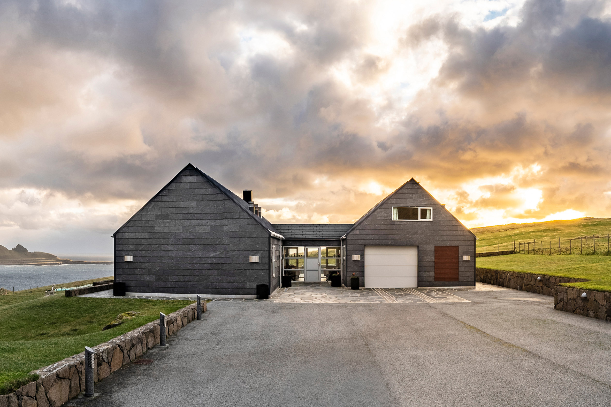 A home made up of two pitched buildings covered in slate cladding with a paved driveway in front