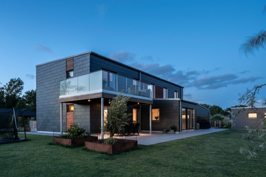 A two-storey home with a slate exterior and balcony with glass balustrades