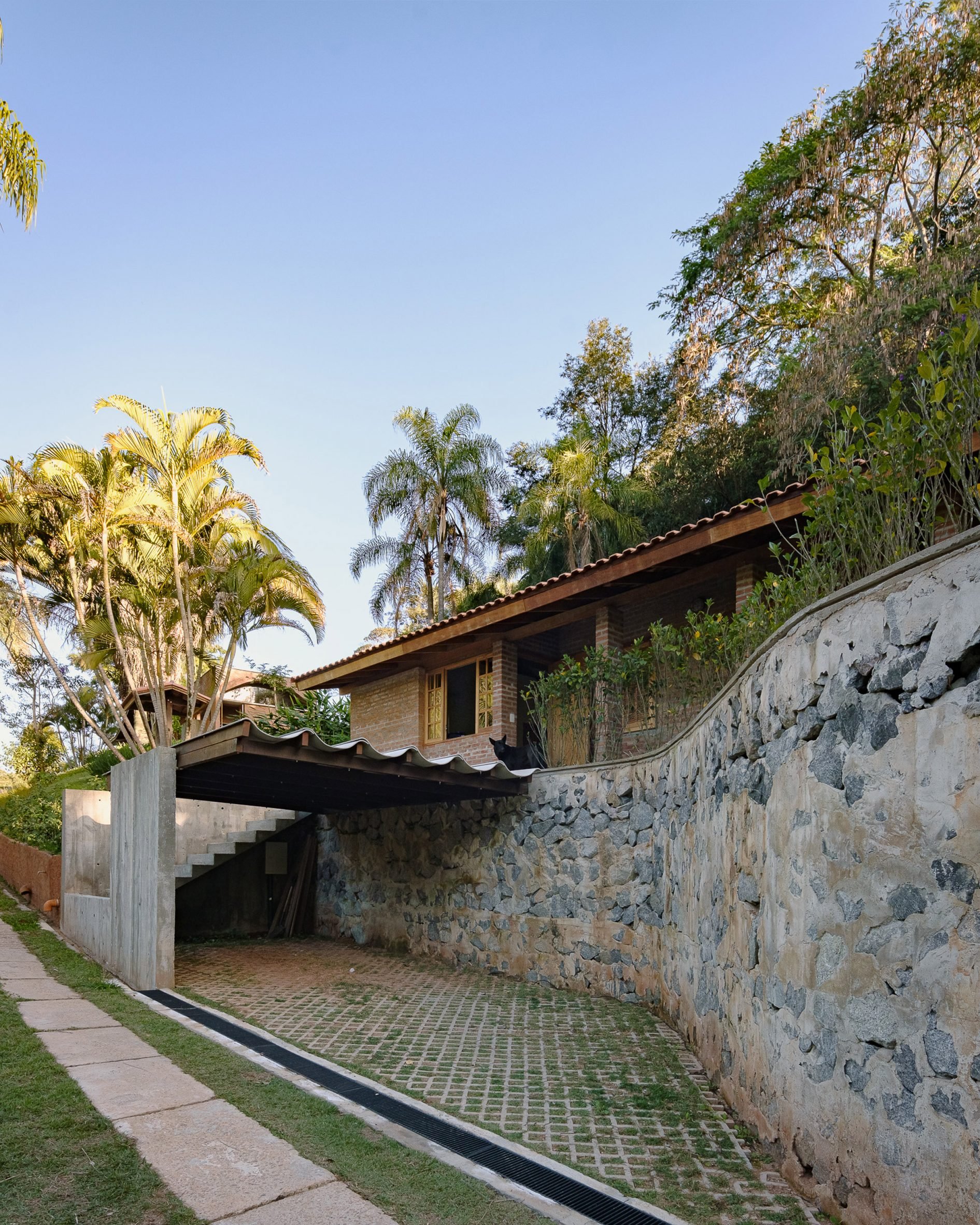 A stone retaining wall outside a brick renovation residential project on a lush site in Brazil