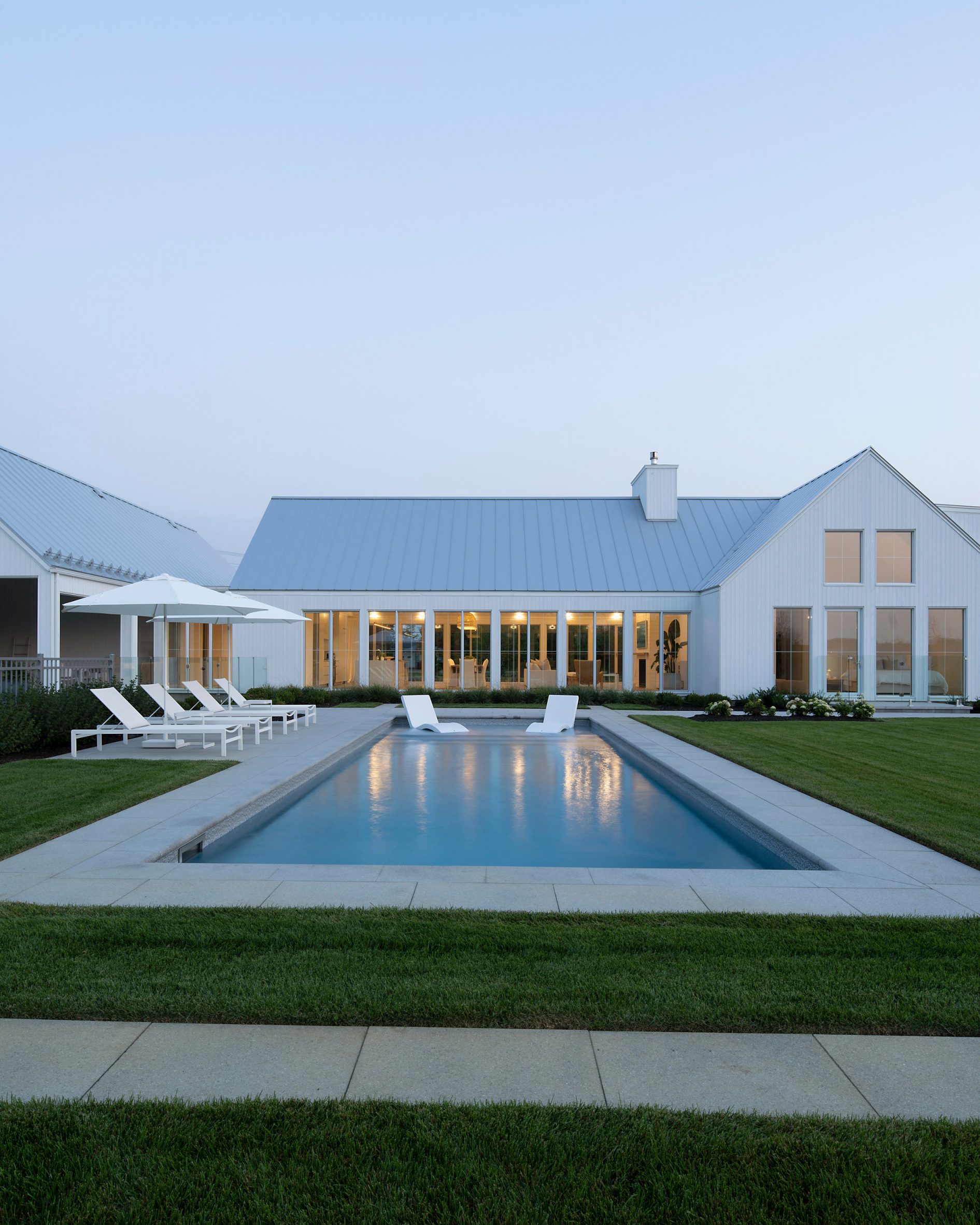 A white U-shaped house with a pitched roof on a green lawn with a swimming pool
