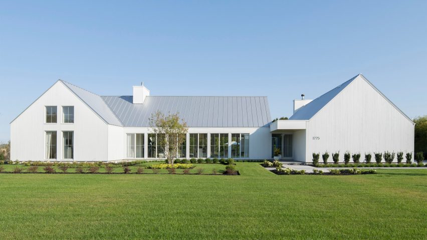 A white U-shaped house with a pitched roof on a green lawn